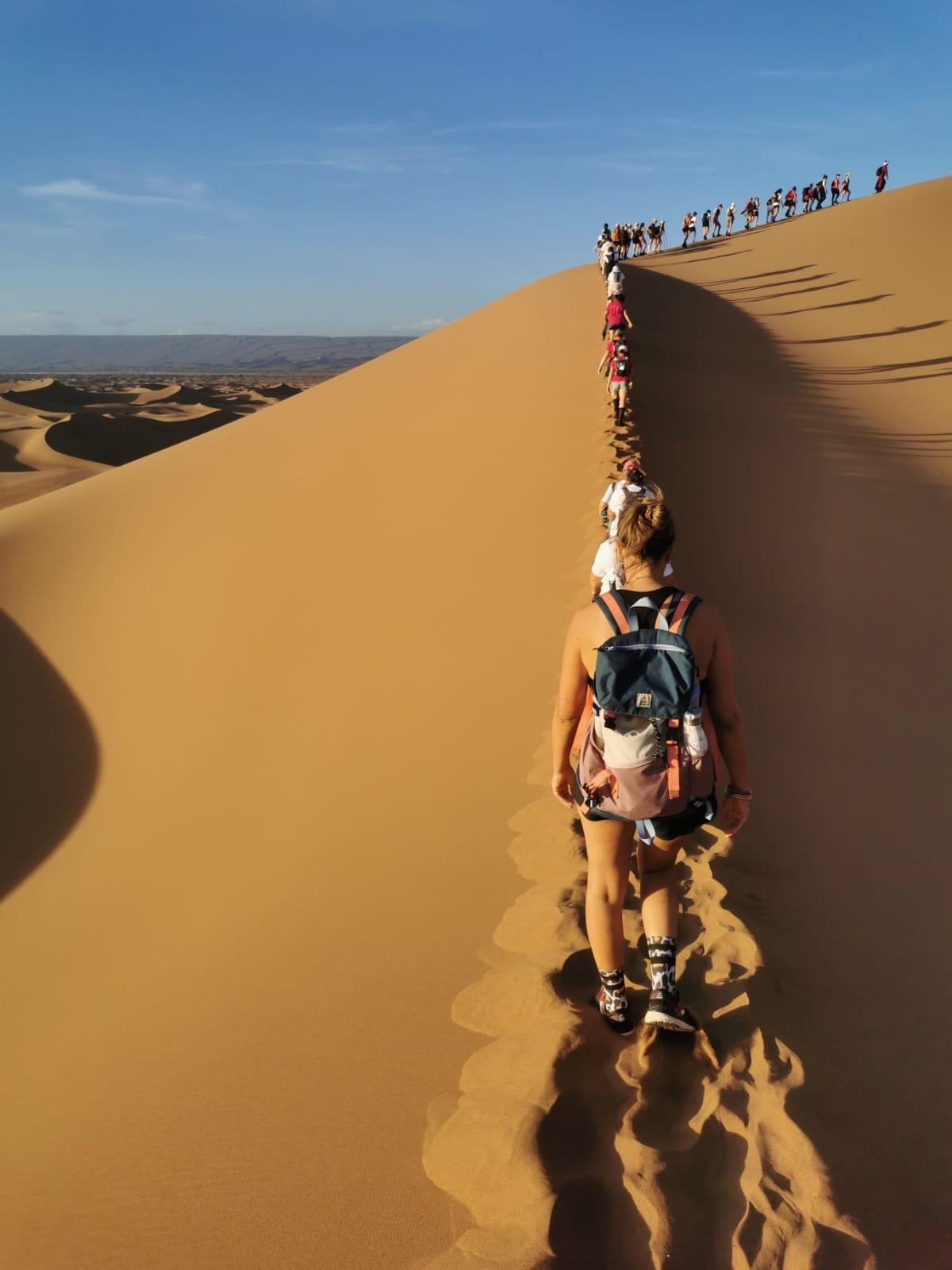 Bivouac désert Maroc — femmes en marche dans les dunes au lever du soleil