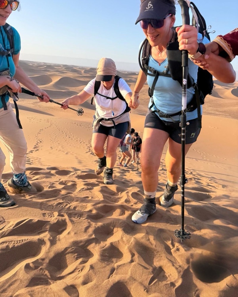 Femmes en trek s'entraidant pour gravir une dune de l'Erg Chegaga, au Maroc, au lever du soleil